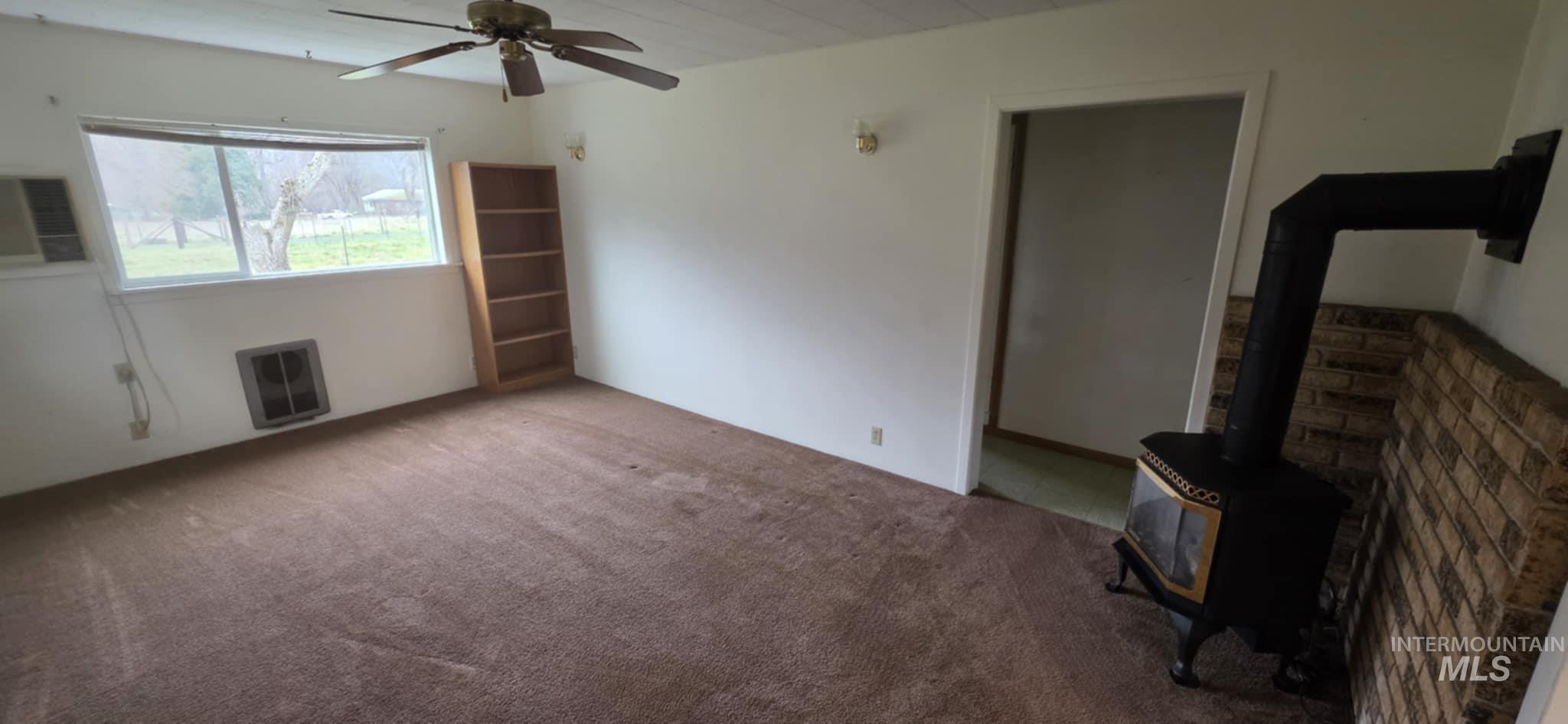 126 Rock Road Kamiah, ID 83536 - Photo 23 of 35 Unfurnished living room featuring a wood stove, heating unit, carpet floors, and ceiling fan