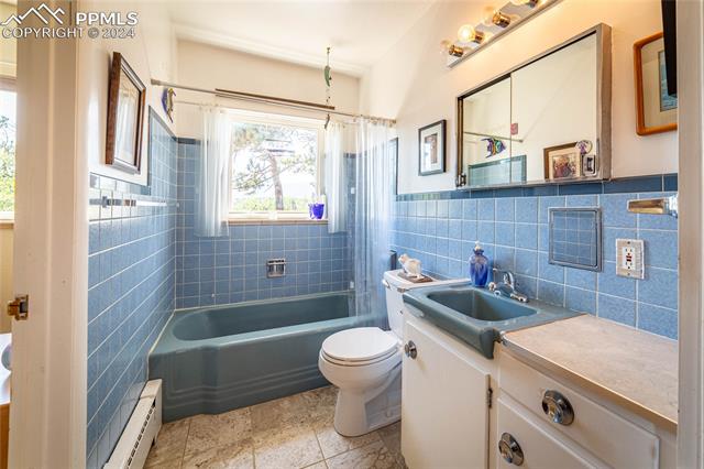 Full bathroom featuring tile walls, backsplash, vanity, toilet, and a baseboard heating unit