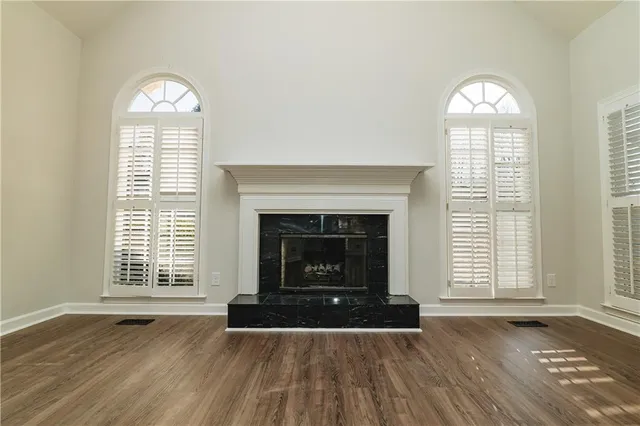 an empty room with wooden floor fireplace and windows
