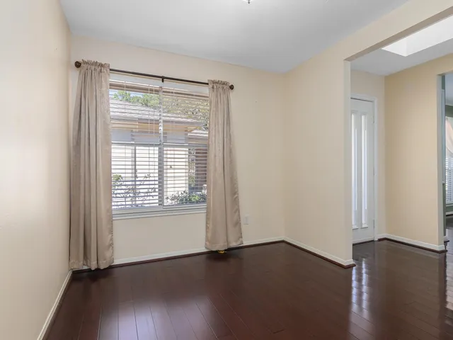 an empty room with wooden floor and windows with curtains