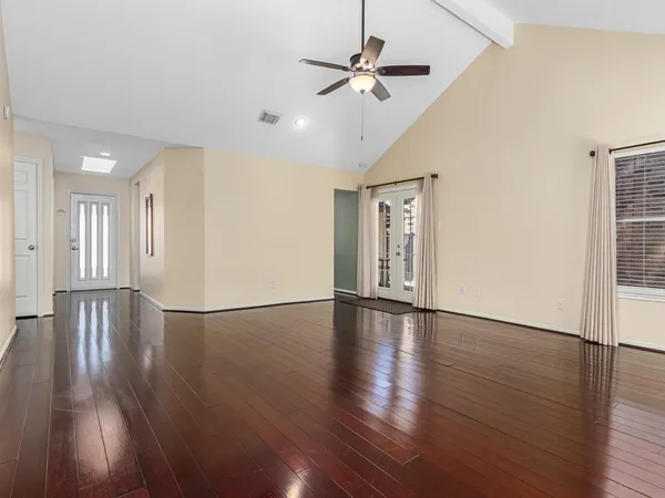 a view of an empty room with wooden floor and a ceiling fan