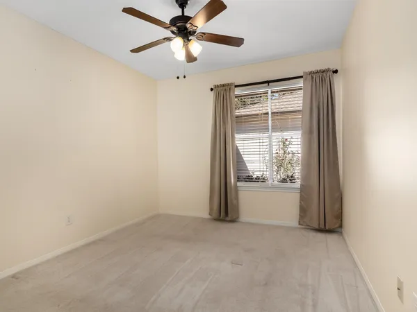 an empty room with chandelier fan and windows