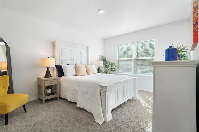 a bed sitting in a spacious bedroom next to a potted plant on a dresser