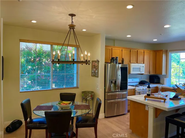 a kitchen area with stainless steel appliances kitchen island granite countertop a dining table chairs and a refrigerator