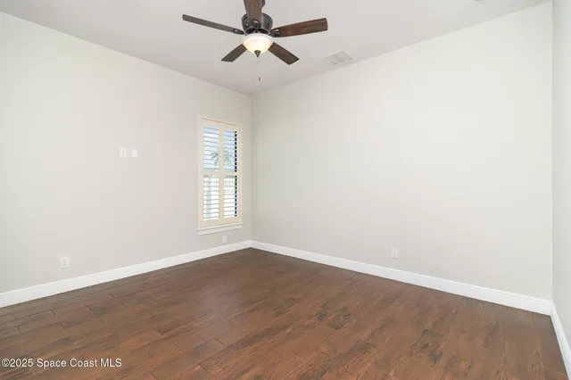 an empty room with wooden floor fan and windows