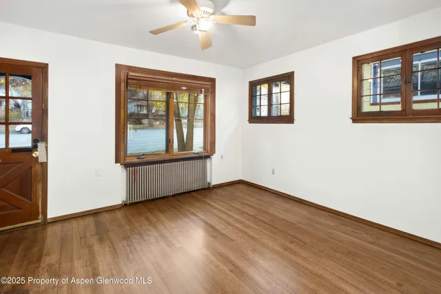 a view of an empty room with wooden floor and fan