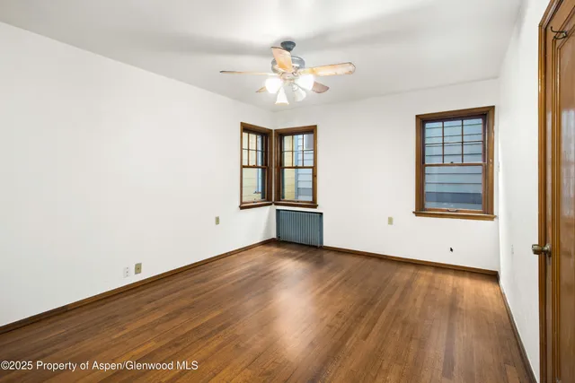 an empty room with wooden floor chandelier and windows