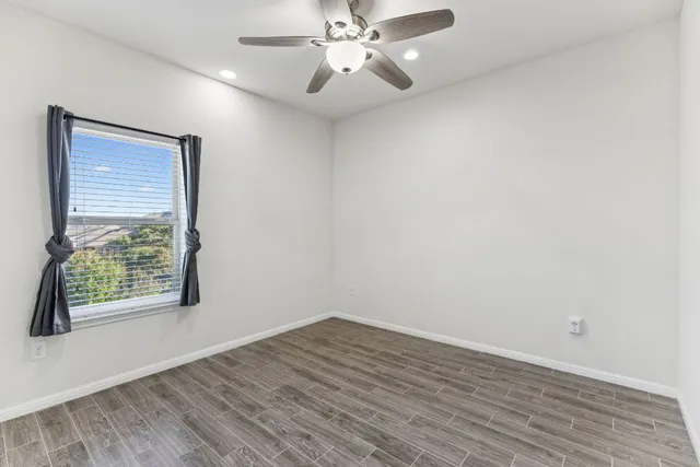 an empty room with wooden floor chandelier fan and windows