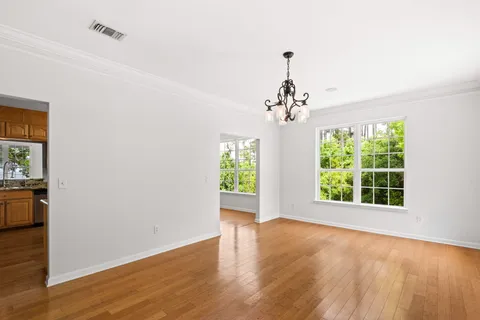 an empty room with wooden floor chandelier and windows