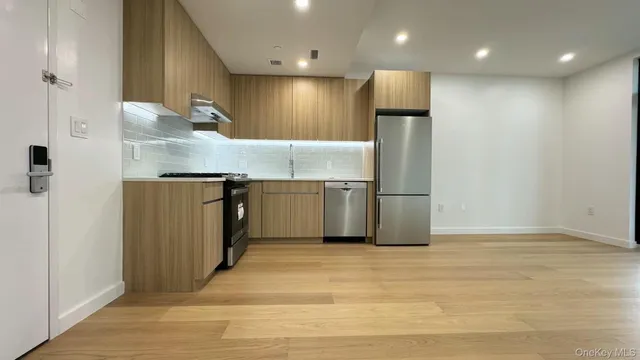 a view of an empty room with wooden floor and a kitchen