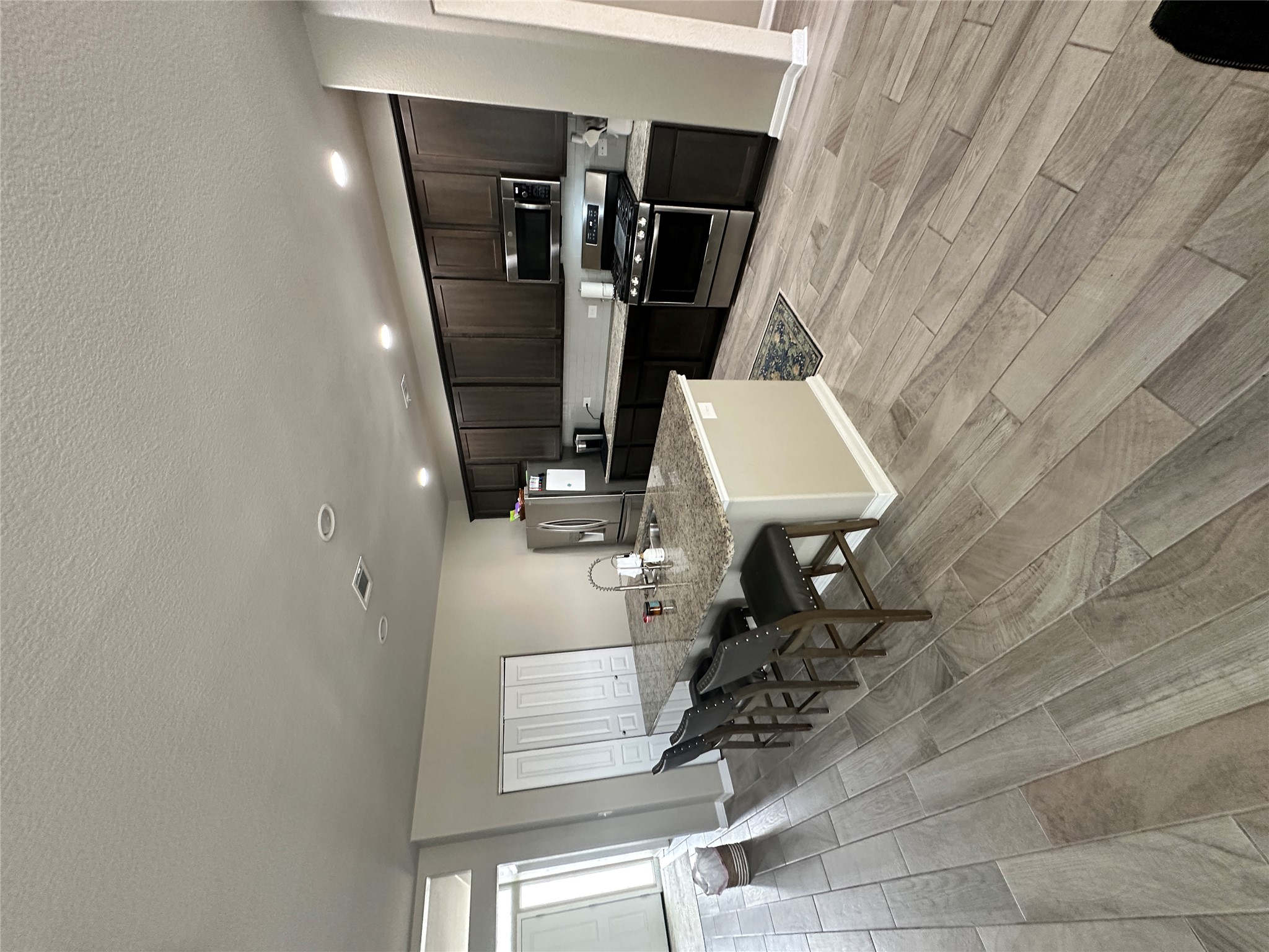 1269 Nevarez Kyle, TX 78640 - Photo 4 of 27 Kitchen with stainless steel appliances, wood tiled floors, an island with sink, a breakfast bar area, and light stone countertops