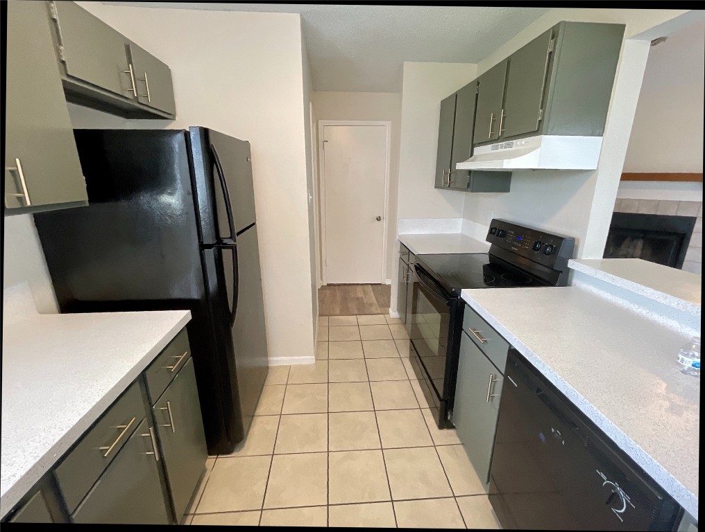 3707 Buffalo Springs Trail, Unit 301 Georgetown, TX 78628 - Photo 7 of 15 Kitchen with black appliances, under cabinet range hood, light tile patterned floors, light stone countertops, and gray cabinets