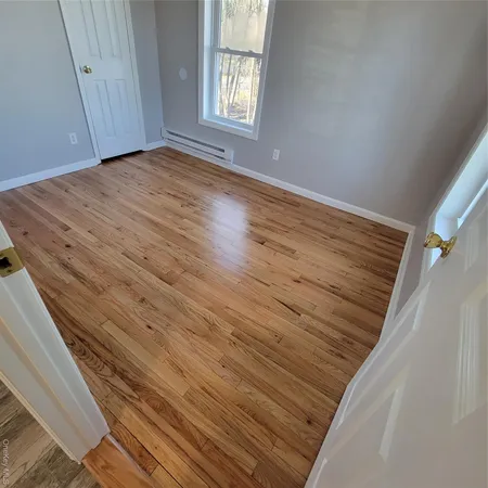 a view of an empty room with wooden floor and a window
