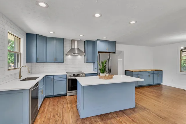 a kitchen with stainless steel appliances granite countertop a sink a stove a refrigerator and a oven with wooden floors