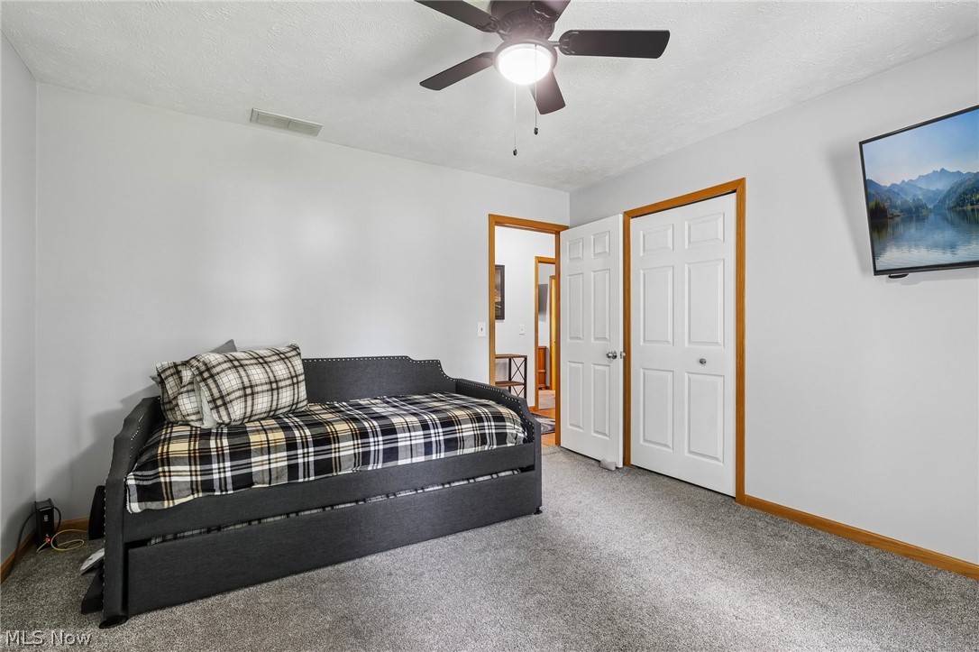 3213 Bates Road Madison, OH 44057 - Photo 28 of 45 Bedroom featuring light gray wall paint, gray carpet flooring, wood trim, white bi-fold closet doors, and a ceiling fan with integrated lighting