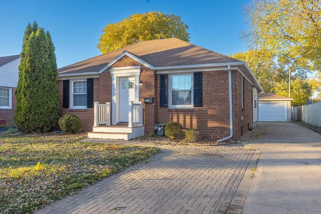 a view of a brick house with a yard plants and large tree