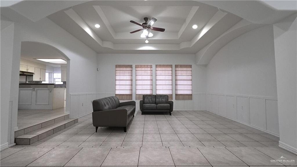2014 Northgate Circle Weslaco, TX 78599 - Photo 4 of 23 Living area featuring a ceiling fan, arched walkways, light tile patterned floors, a tray ceiling, and a wainscoted wall