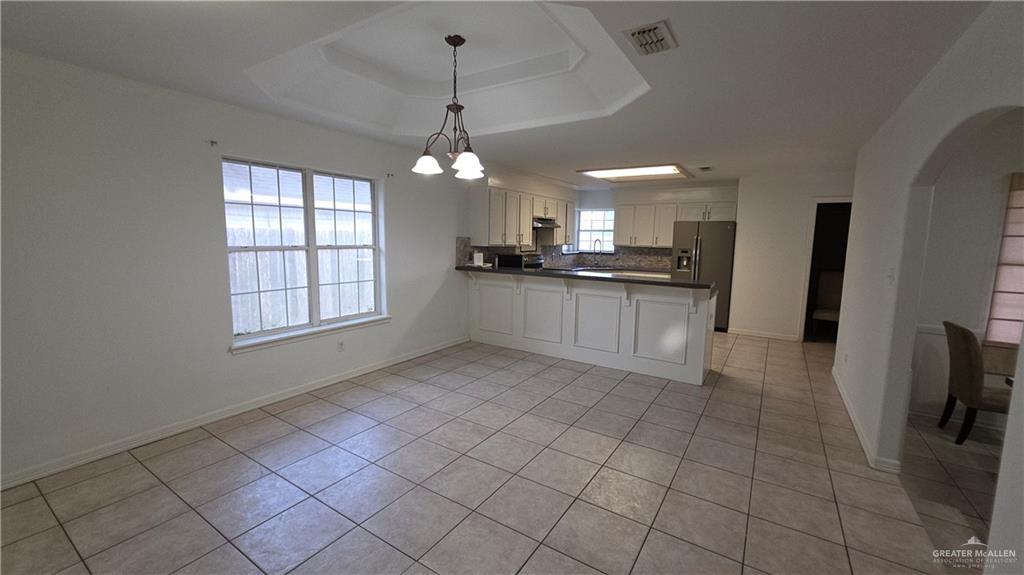 2014 Northgate Circle Weslaco, TX 78599 - Photo 7 of 23 Kitchen featuring dark countertops, a raised ceiling, a chandelier, a peninsula, and light tile patterned flooring