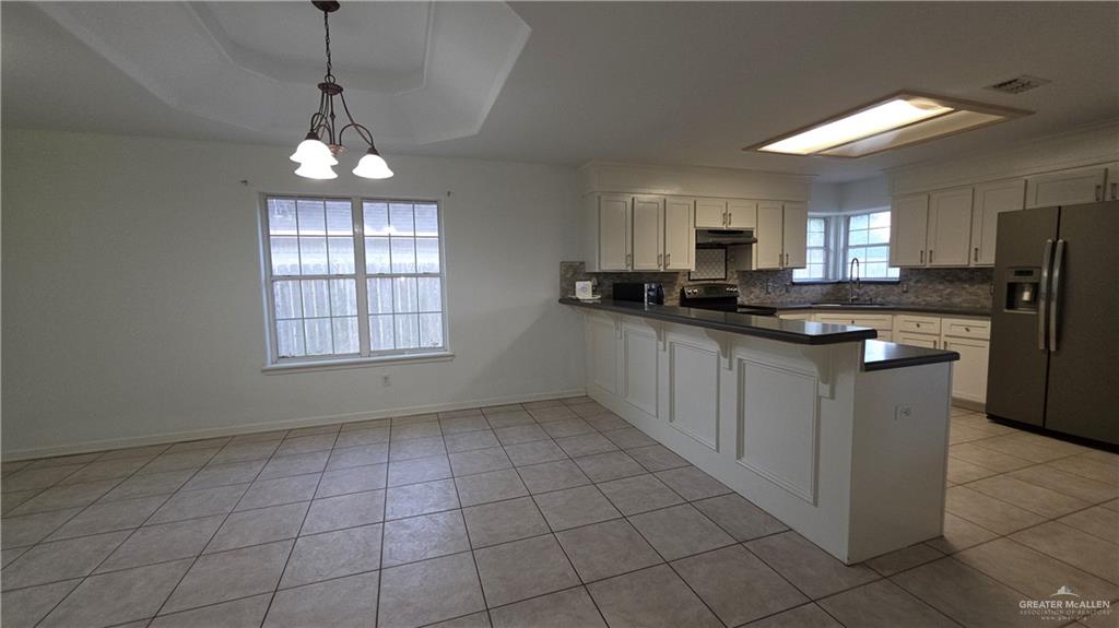 2014 Northgate Circle Weslaco, TX 78599 - Photo 8 of 23 Kitchen with dark countertops, stainless steel fridge with ice dispenser, decorative backsplash, a peninsula, and a raised ceiling