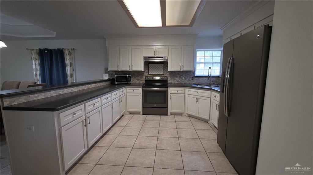 2014 Northgate Circle Weslaco, TX 78599 - Photo 9 of 23 Kitchen featuring stainless steel appliances, light tile patterned flooring, decorative backsplash, white cabinets, and a peninsula