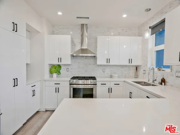 a kitchen with stainless steel appliances a sink a stove a chimney a refrigerator and cabinets