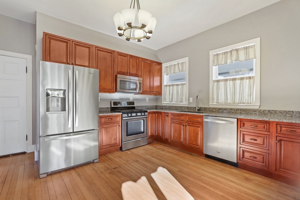 a kitchen with stainless steel appliances granite countertop a refrigerator a stove top oven a sink and dishwasher with wooden floor