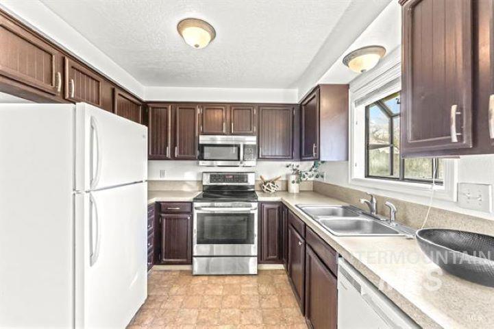 2481 West Rebecca Way Meridian, ID 83646 - Photo 5 of 17 Kitchen featuring stainless steel appliances, light countertops, dark wood finish cabinets, and a textured ceiling