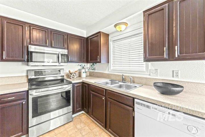 2481 West Rebecca Way Meridian, ID 83646 - Photo 6 of 17 Kitchen with stainless steel appliances, light countertops, dark wood finish cabinets, and a textured ceiling