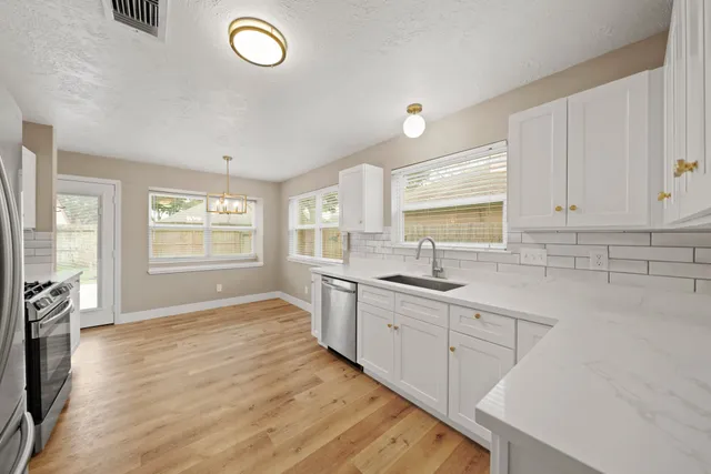 a kitchen with granite countertop a stove a sink and white cabinets with wooden floor