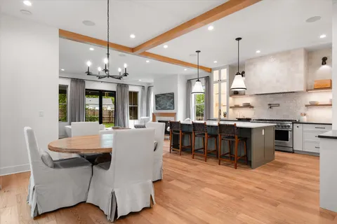 a kitchen with stainless steel appliances granite countertop a stove a refrigerator a sink a dining table and chairs with wooden floor