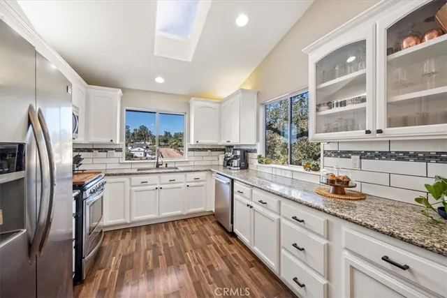 a kitchen with stainless steel appliances granite countertop a refrigerator a stove top oven a sink and dishwasher with wooden floor