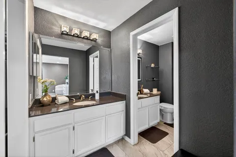 a spacious en suite bathroom with a granite countertop sink and a mirror