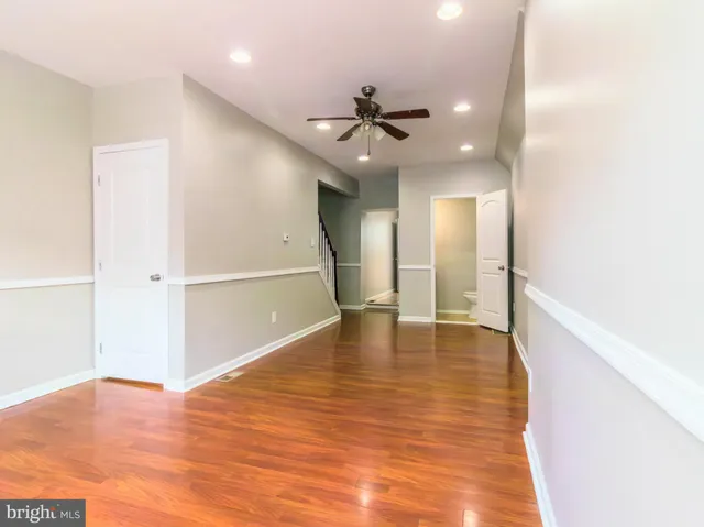a view of an empty room with wooden floor and a ceiling fan
