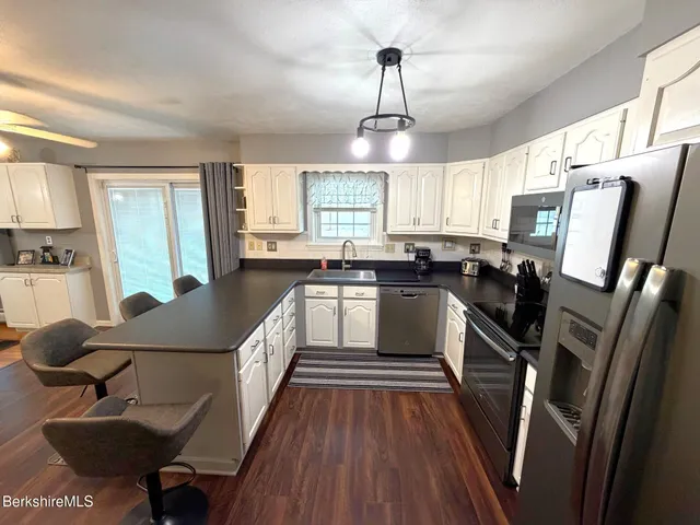 a kitchen with granite countertop a refrigerator a sink dishwasher a stove and white countertops with wooden floor