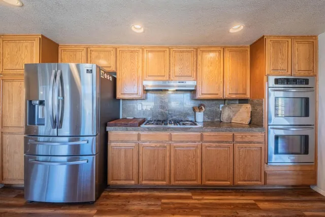 a kitchen with stainless steel appliances granite countertop a refrigerator a stove and a sink with wooden floor
