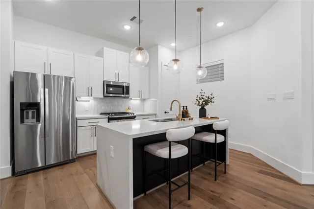 a kitchen with stainless steel appliances granite countertop a sink a stove a refrigerator and island with wooden floor