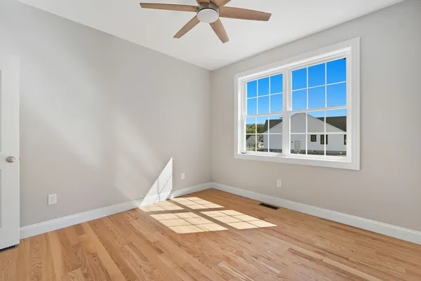 a view of empty room with wooden floor and fan