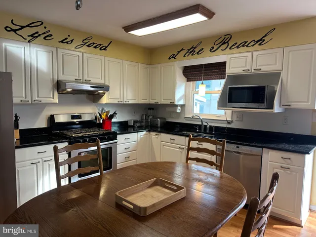 a kitchen with stainless steel appliances granite countertop a stove a sink dishwasher a microwave oven and a dining table with wooden cabinet