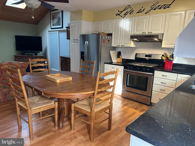 a kitchen with stainless steel appliances a stove a sink dishwasher a refrigerator cabinets and a dining table with wooden floor