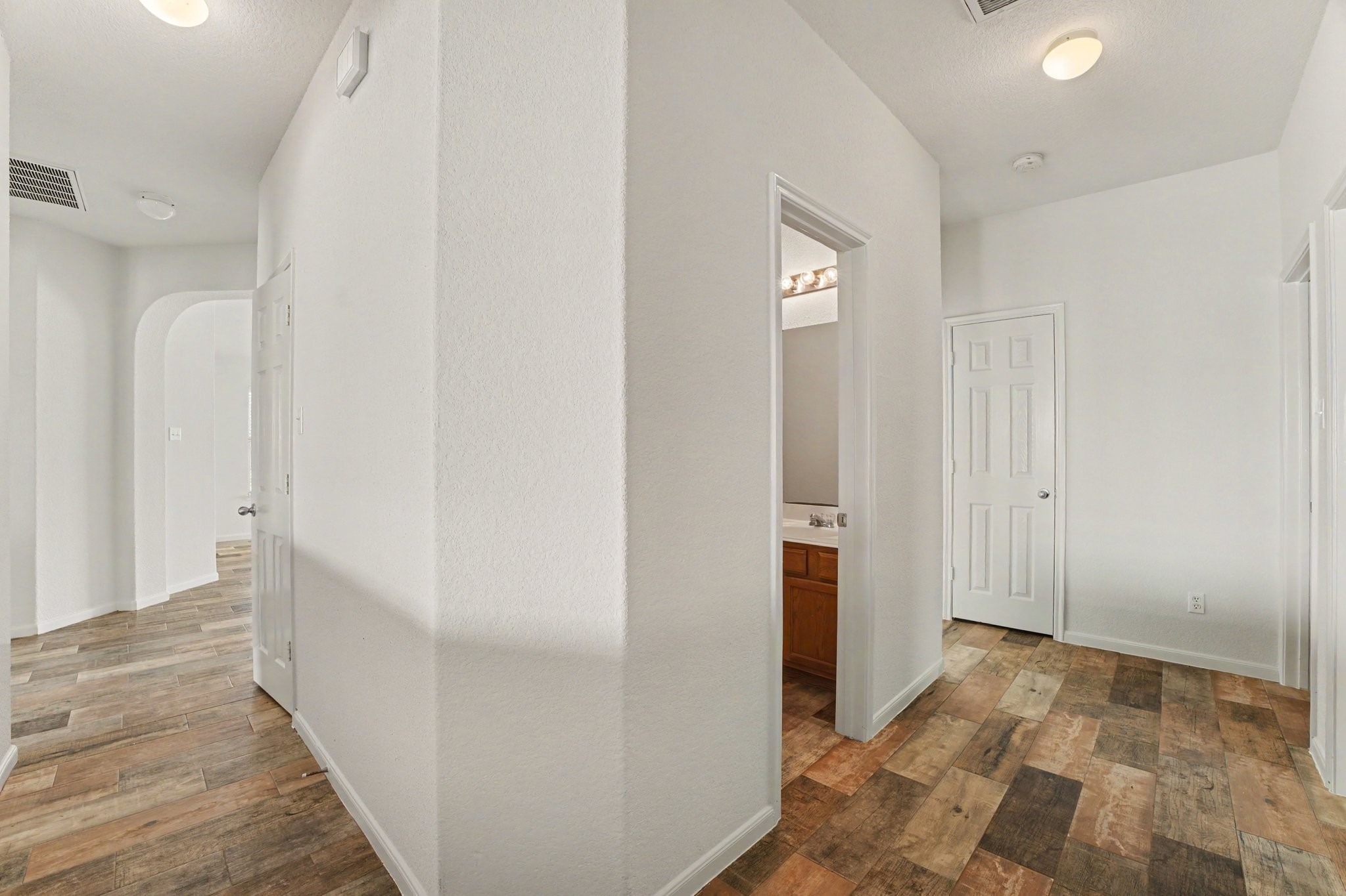 21427 Blooming Rock Lane Spring, TX 77379 - Photo 24 of 32 This photo showcases a bright, clean hallway with white walls and wood-look tile flooring. The space has multiple doorways and a bathroom entrance, providing a spacious and inviting layout.