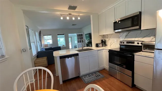 a kitchen with stainless steel appliances granite countertop a stove top oven a sink dishwasher and white cabinets with wooden floor