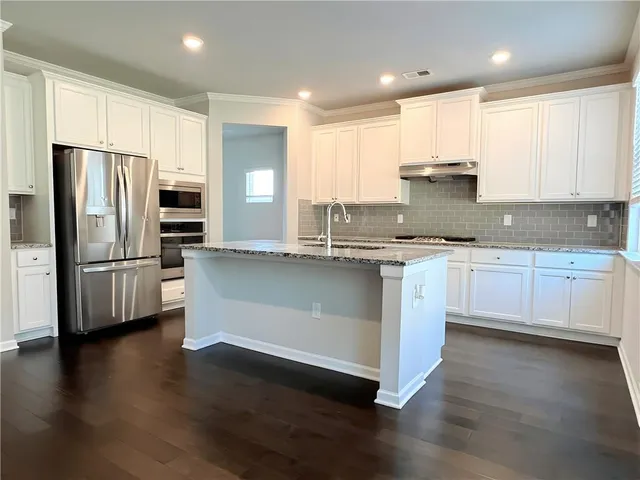 a kitchen with stainless steel appliances granite countertop a refrigerator a sink dishwasher a stove and white cabinets with wooden floor