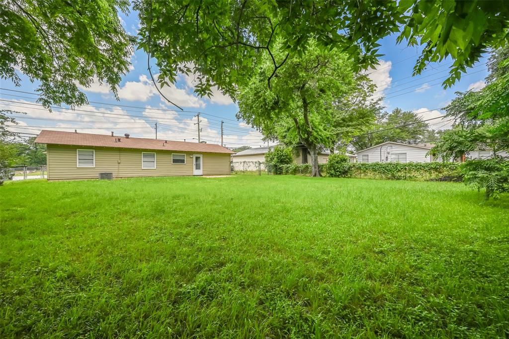1905 South Cooper Street Arlington, TX 76010 - Photo 15 of 15 Expansive green lawn with mature trees and a single-story residence featuring light-toned siding, multiple windows, and a rear entry door