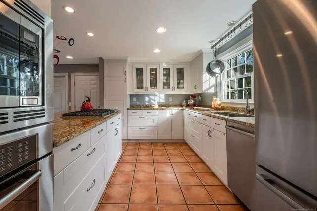 a kitchen with stainless steel appliances granite countertop a stove a sink a oven with white cabinets and wooden floor