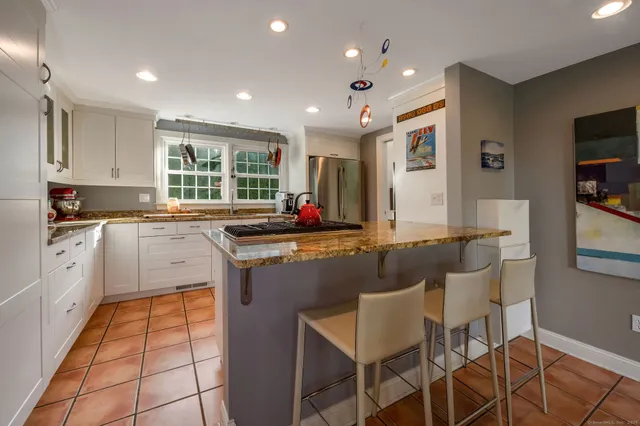 a kitchen with stainless steel appliances kitchen island granite countertop dining table chairs and a refrigerator