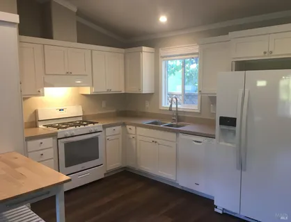 a kitchen with granite countertop white cabinets appliances a sink and a window