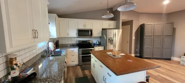 a room with stainless steel appliances kitchen island granite countertop a refrigerator a stove top oven a sink and dishwasher