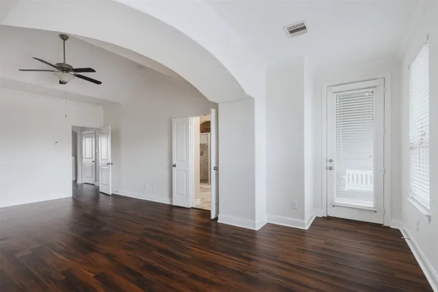 an empty room with wooden floor ceiling fan and windows