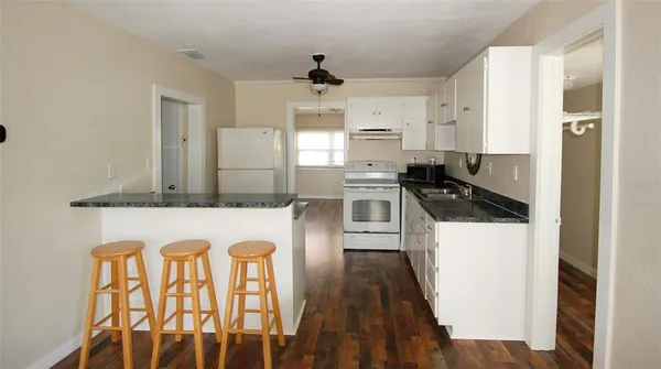 a kitchen with stainless steel appliances granite countertop a refrigerator a stove a sink and white cabinets with wooden floor