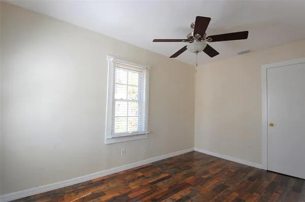 an empty room with wooden floor fan and windows
